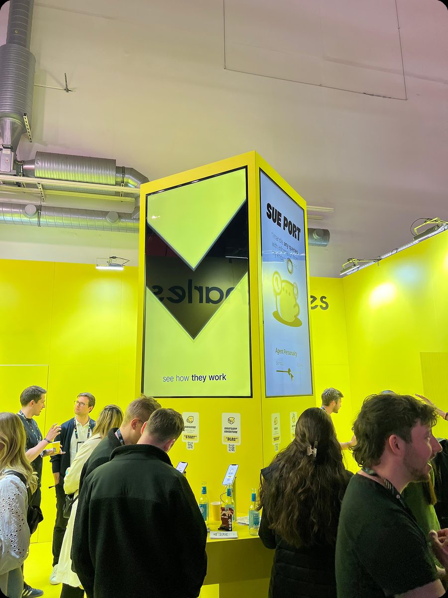 Trade-fair booth with a yellow interactive info pillar and visitors
